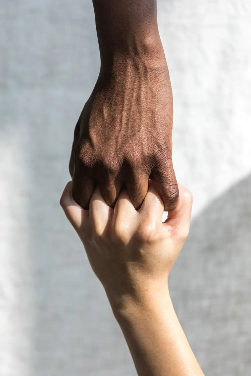Two hands, one darker-skinned and one lighter-skinned, clasped together in a gentle grip.